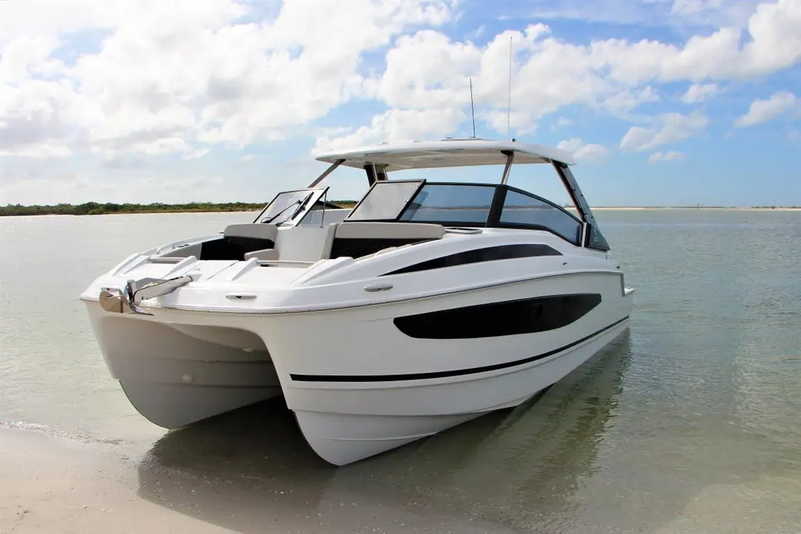 A modern white boat with black accents anchored in shallow water, surrounded by a sandy shoreline and blue skies.